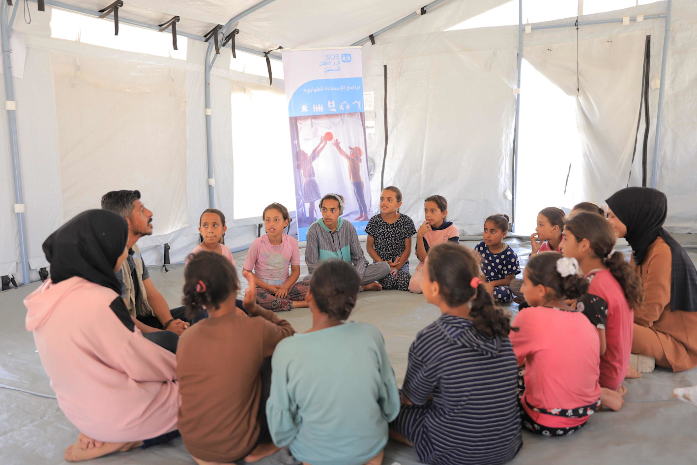 Children and carers from SOS Children's Villages sitting in a circle in the Khan Younis emergency camp