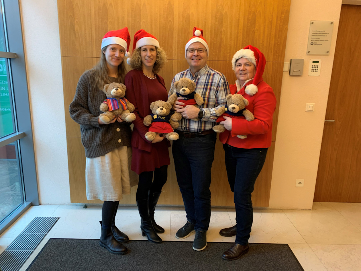 Das SOS-Kinderdorf Liechtenstein Team mit Weihnachtsmützen und den Teddybären Finn und Fina. 