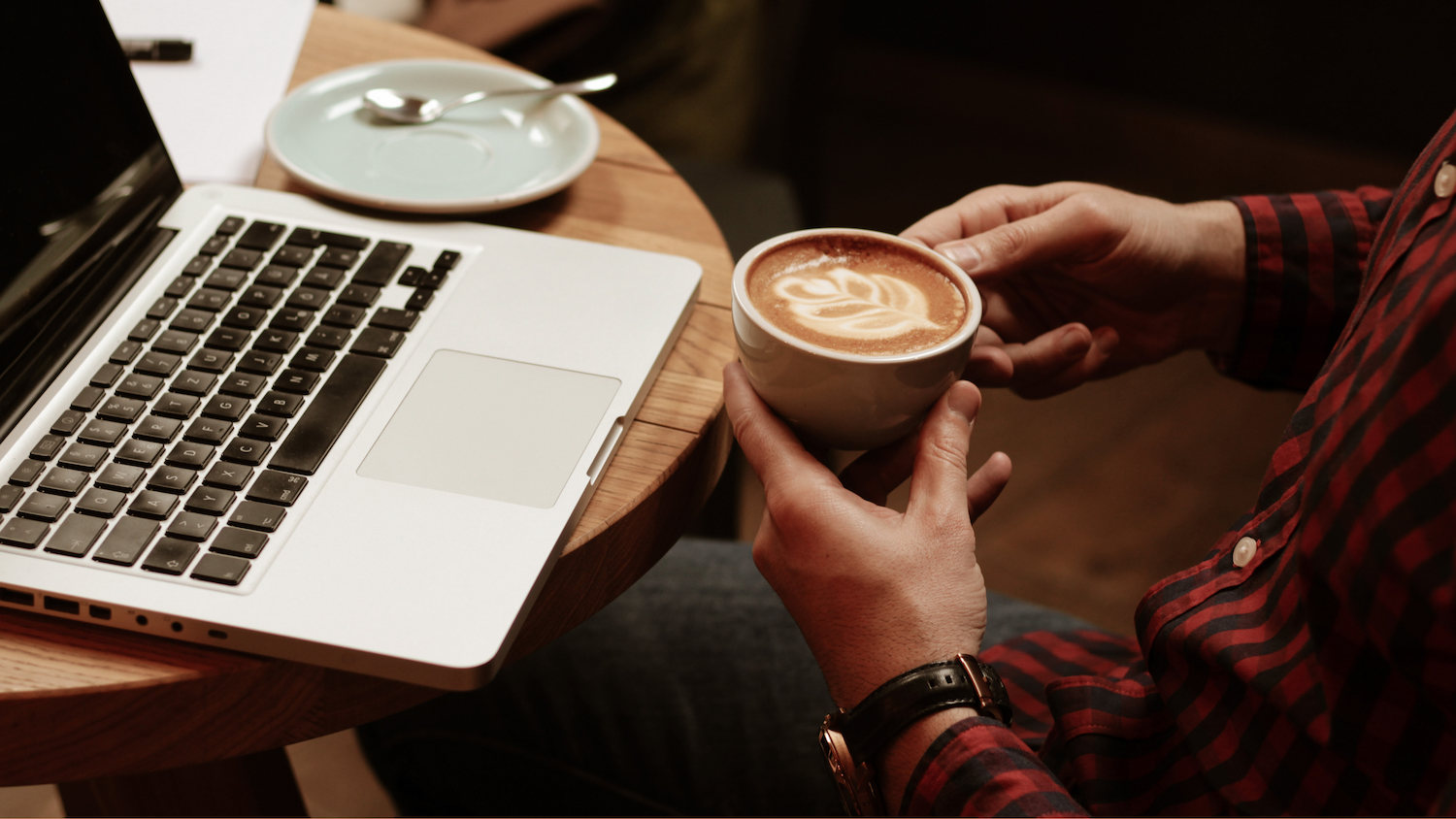 A man drinking coffee while working on a laptop in a cafe.