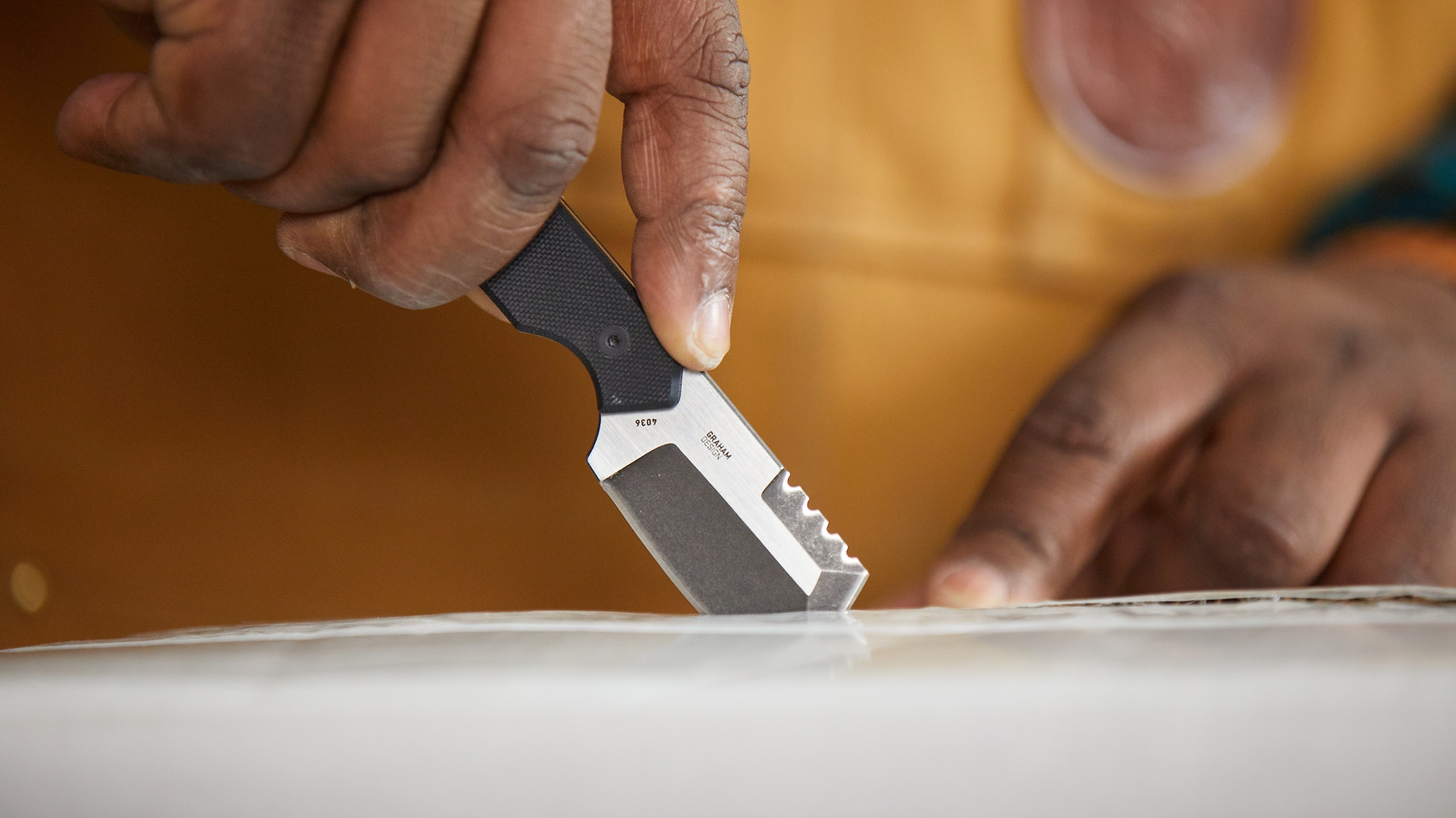 Close up of man using a knife to slice a smooth material.