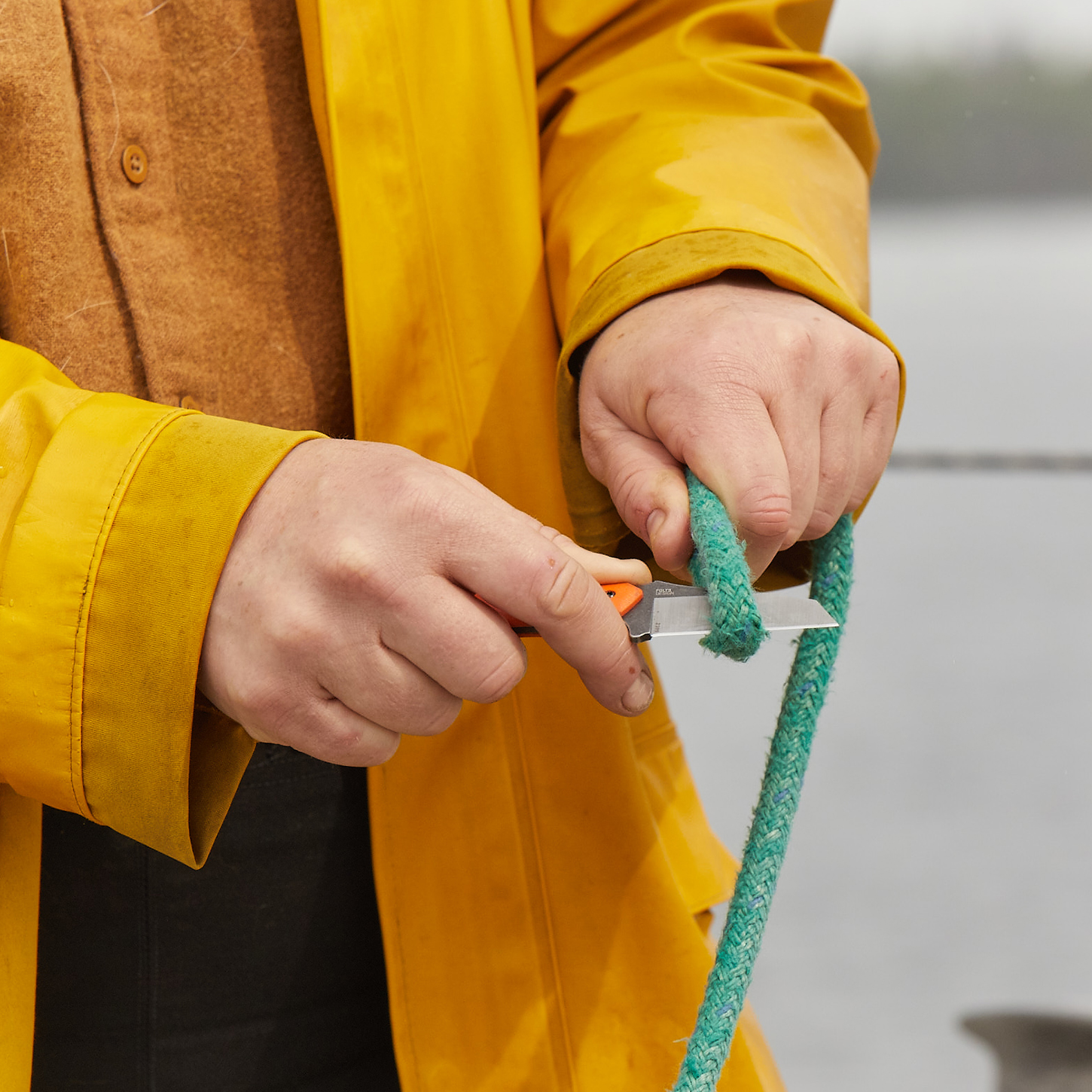 Woman in yellow jacket cutting rope with knife.