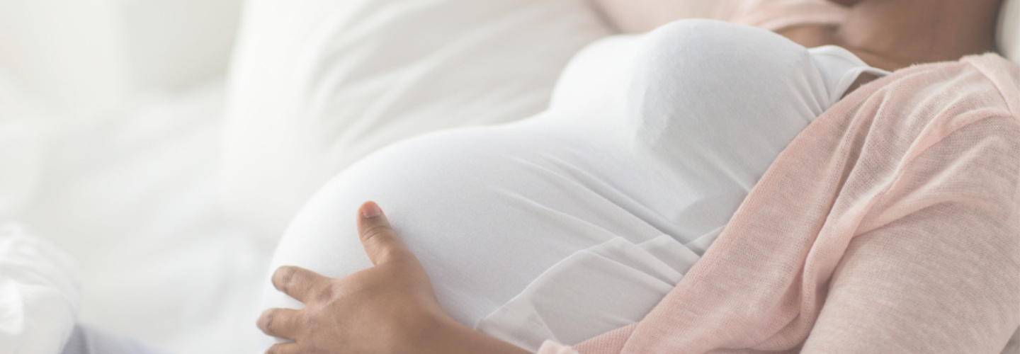 Bilden visar kroppen av en gravid person där händer håller om magen.