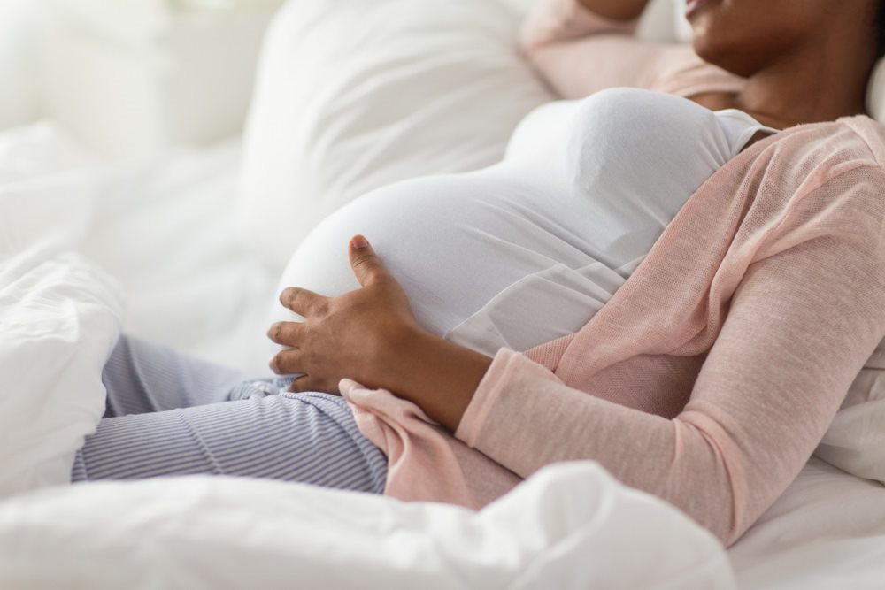 Bilden visar kroppen av en gravid person där händer håller om magen.