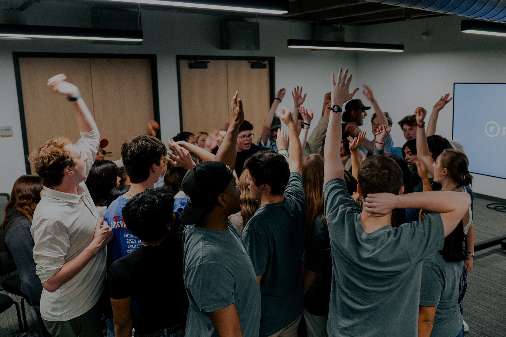 High school students raising their hands in celebration during a Re:generation for Students group session at Watermark Community Church in Dallas, Texas.