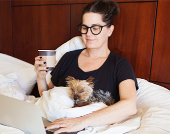 Femme assise dans son lit avec chien et café et ordinateur
