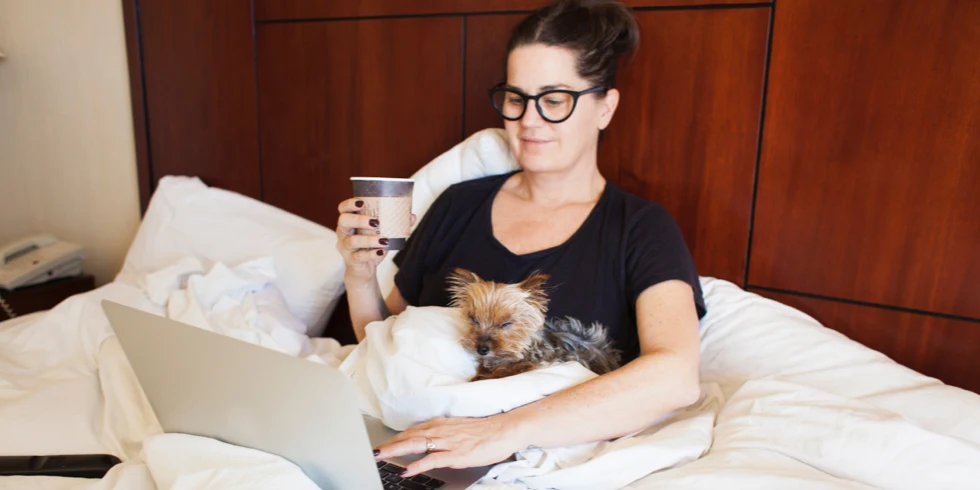 Femme assise dans son lit avec chien et café et ordinateur