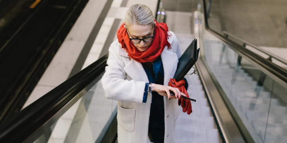 Femme bien habillée avec un portefeuille d’affaires debout sur un escalator