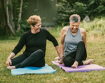 Deux femmes sur des tapis de yoga à l’extérieur en riant et en faisant de l’exercice