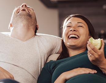 Couple enceinte riant sur le canapé