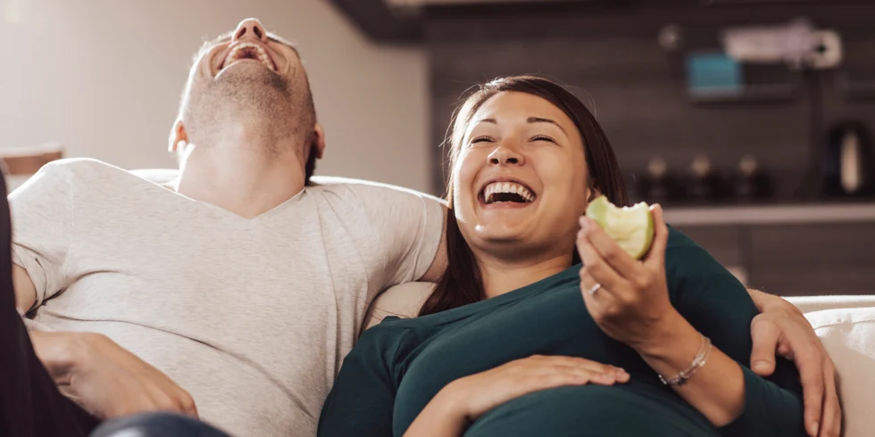 Couple enceinte riant sur le canapé