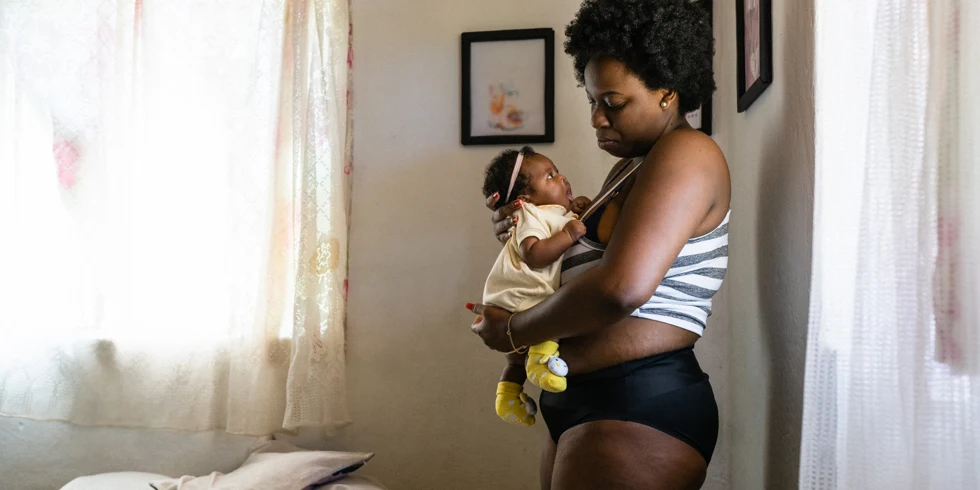 Mère en post-partum portant une culotte noire et tenant un jeune bébé dans ses bras
