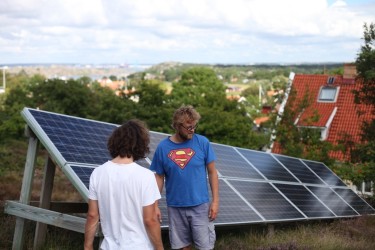 Erik Wallnér och Jörgen Larsson, iförd en Stålmannen-tröja, står vid Jörgens solcellsanläggning som han har satt upp på berghällen bakom sitt hus