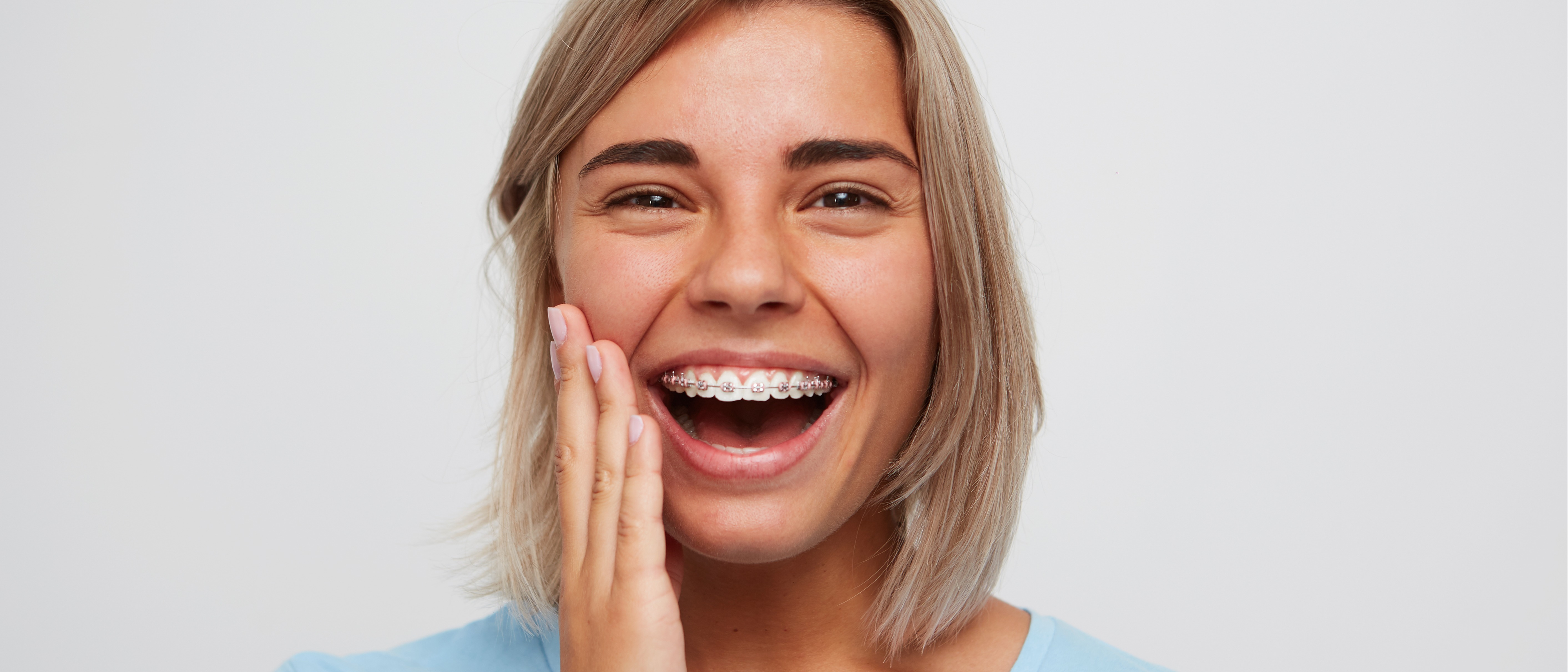 Youg woman with braces holding her jaw and smiling