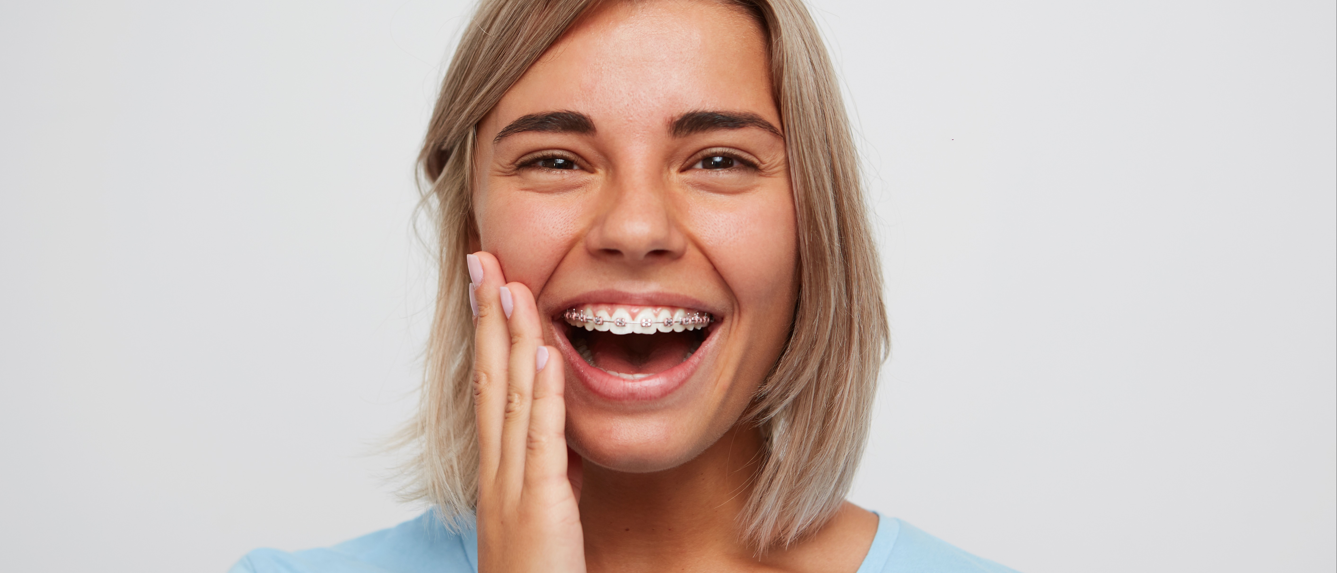 Jeune femme avec un appareil orthodontique se tenant la mâchoire et souriant