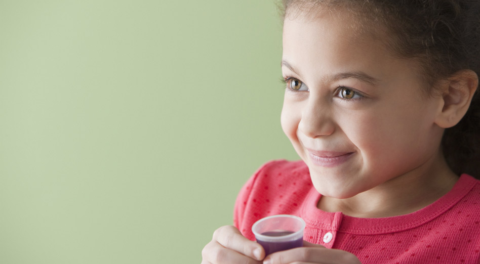 Little girl holding a small cup of liquid medication 