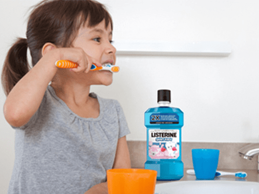 petite fille se brossant les dents, avec un flacon de rince-bouche Listerine sur le comptoir