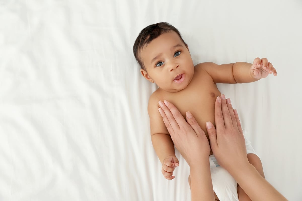 Bébé allongé sur un lit blanc avec sa couche et se faisant appliquer de la lotion pour bébés.