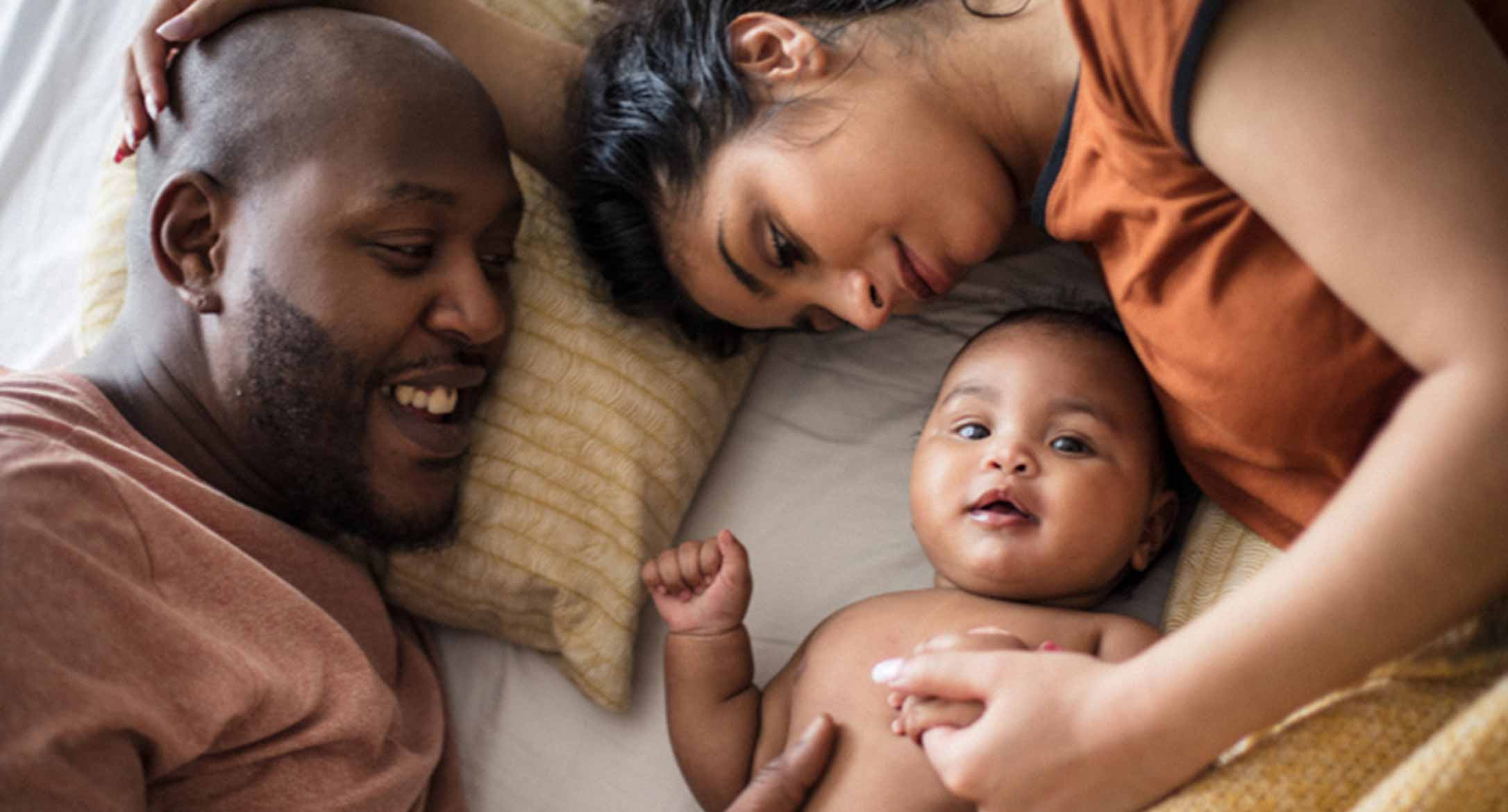 A dad, a mum laying on bed with their new born baby