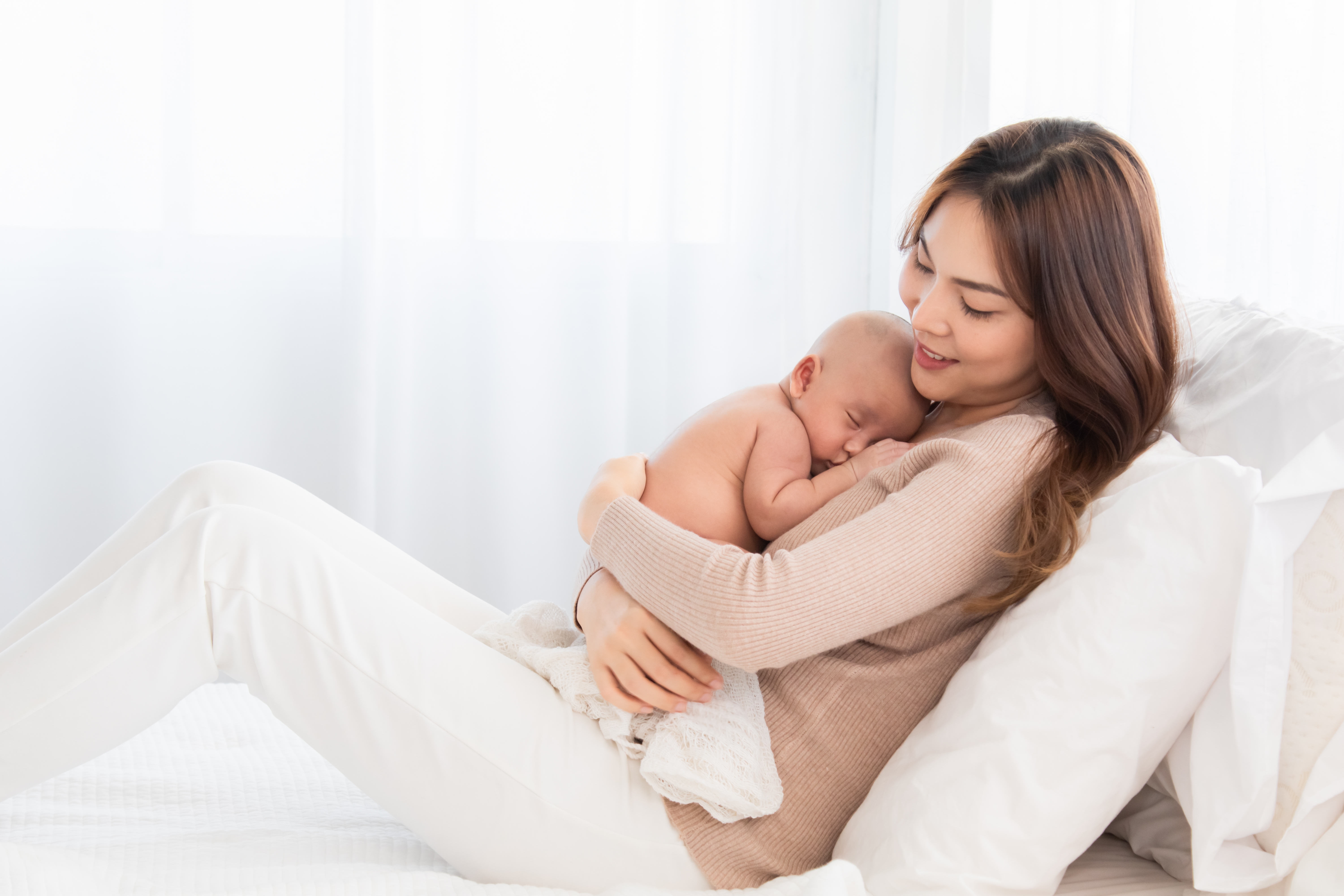 Femme assise sur un lit, qui tient son nouveau-né dans ses bras.