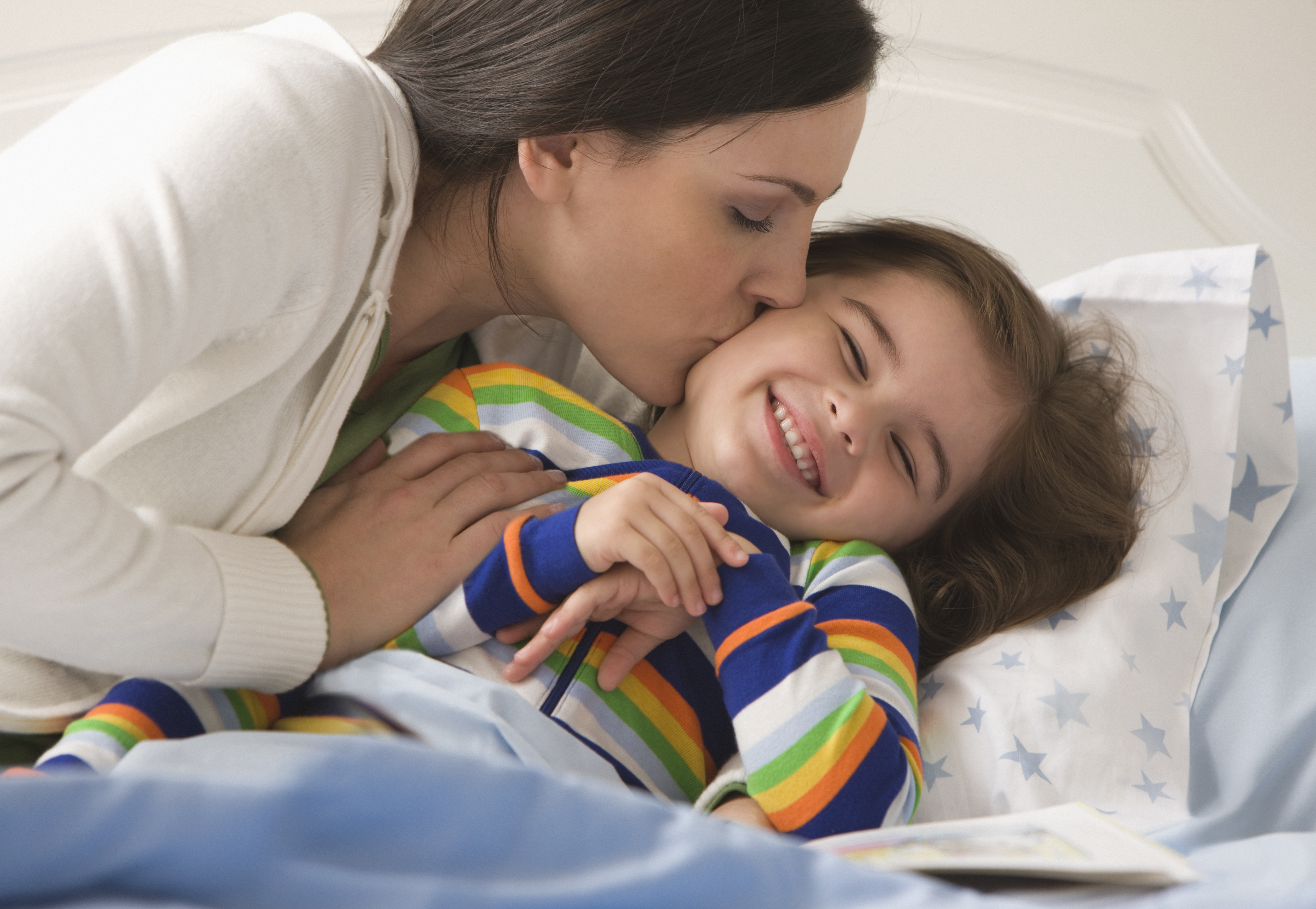 Woman giving her little daughter a kiss on the cheek before bed