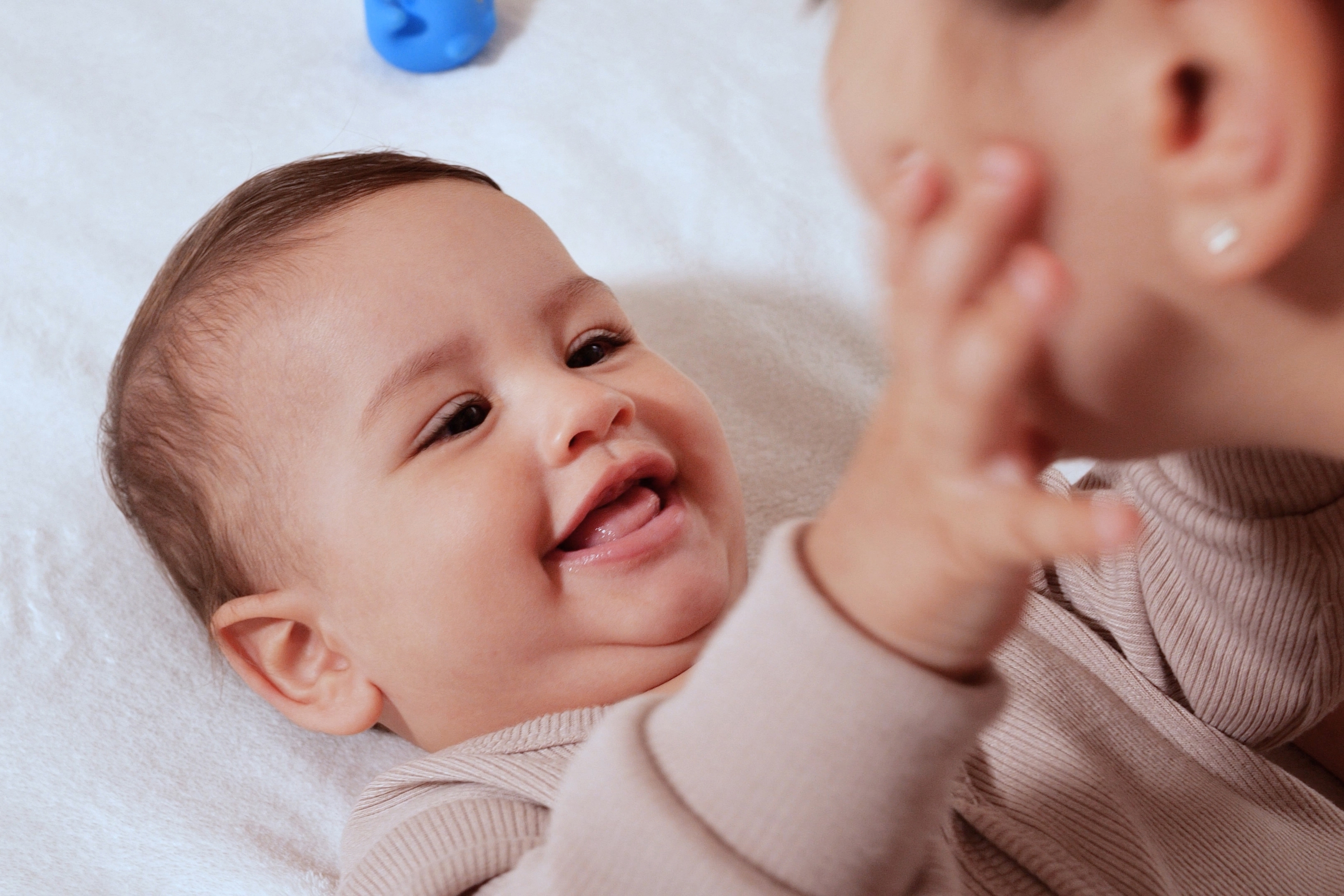 Bébé allongé qui sourit en touchant le visage de sa maman.