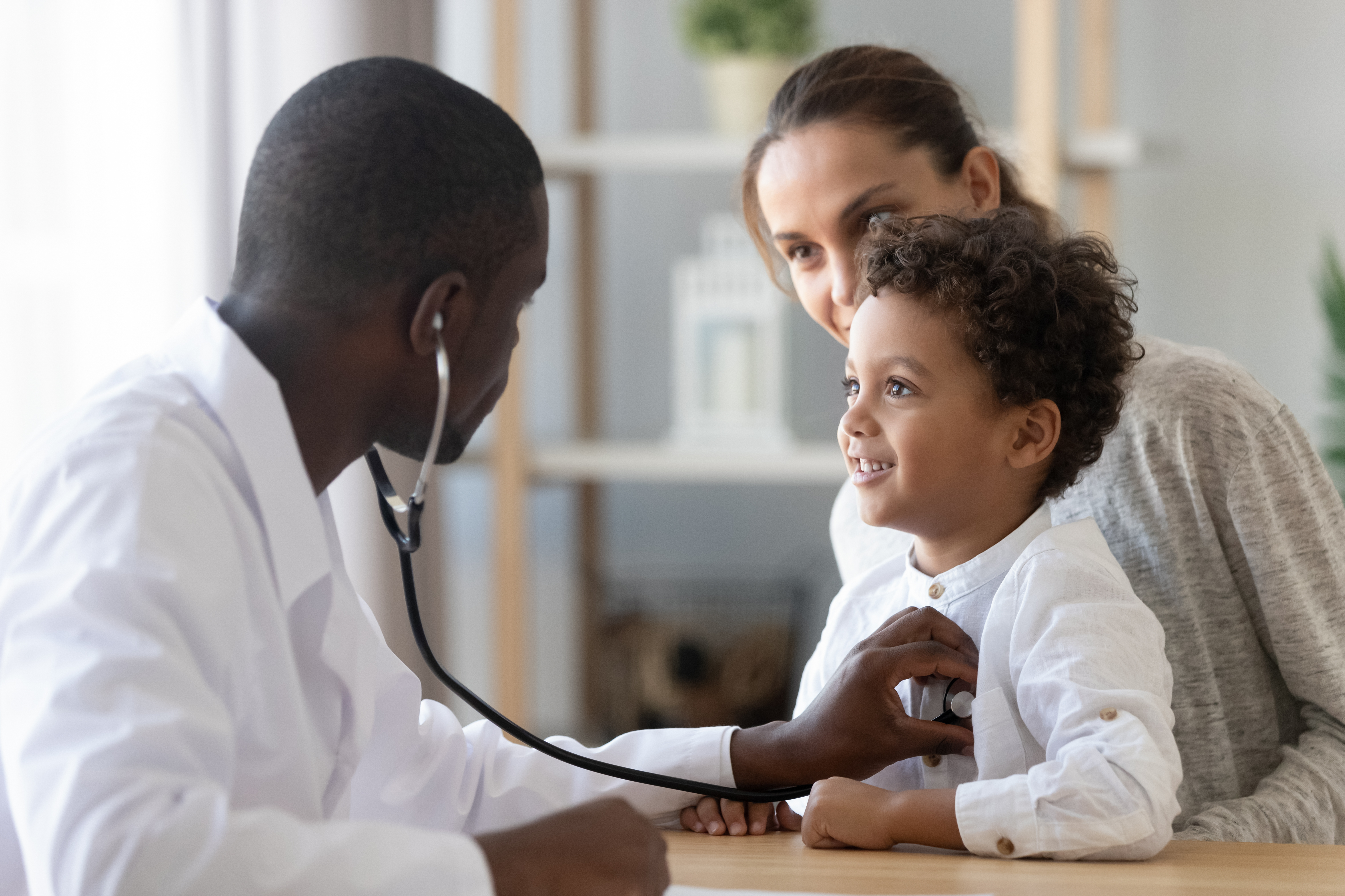 Doctor checking the heartbeat of a little boy who is sitting on his mother’s lap