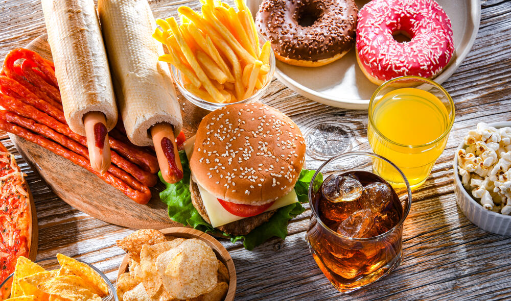 Une bannière présentant des aliments et des boissons acides comme des hamburgers, des frites et du jus d’orange qui peuvent causer des dents sensibles