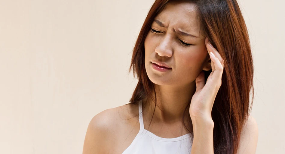 Woman with closed eyes having a migraine and holding her left temple with her hand