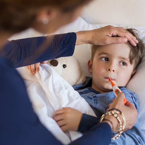 Mère qui prend la température de son petit garçon à l’aide d’un thermomètre buccal