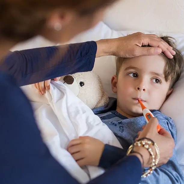 Mère qui prend la température de son petit garçon à l’aide d’un thermomètre buccal