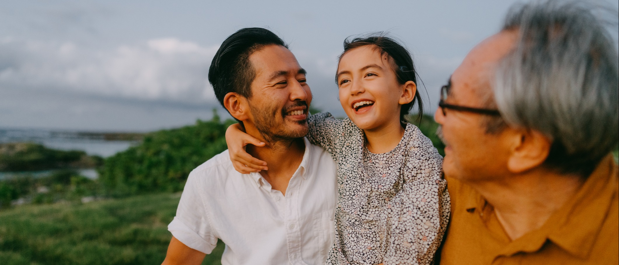 Jeune fille souriante assise sur les genoux de son père à côté de son grand-père à l’extérieur