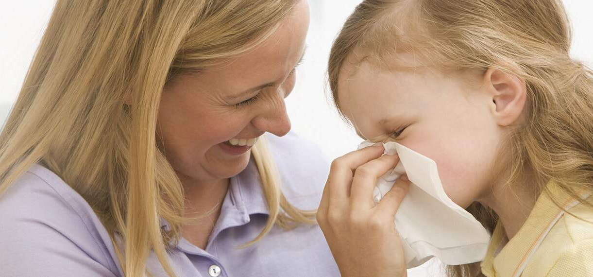 Mother helping daughter blow her nose and handle cold symptoms with MOTRIN®