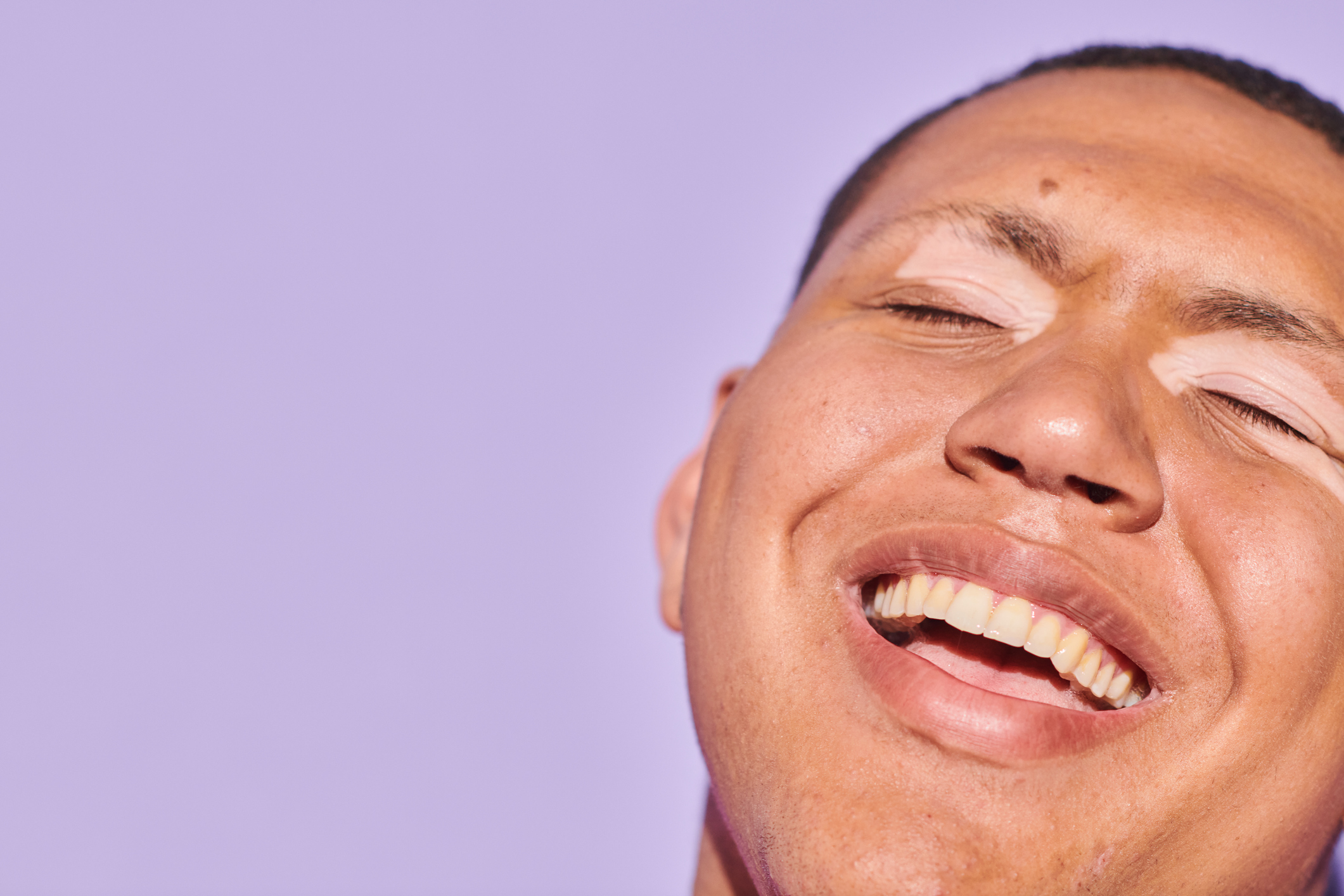 Young man with closed eyes smiling  with his teeth showing 