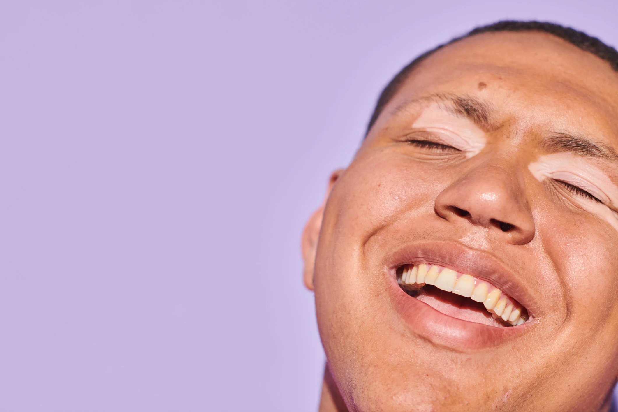 Jeune homme souriant à pleines dents, les yeux fermés 