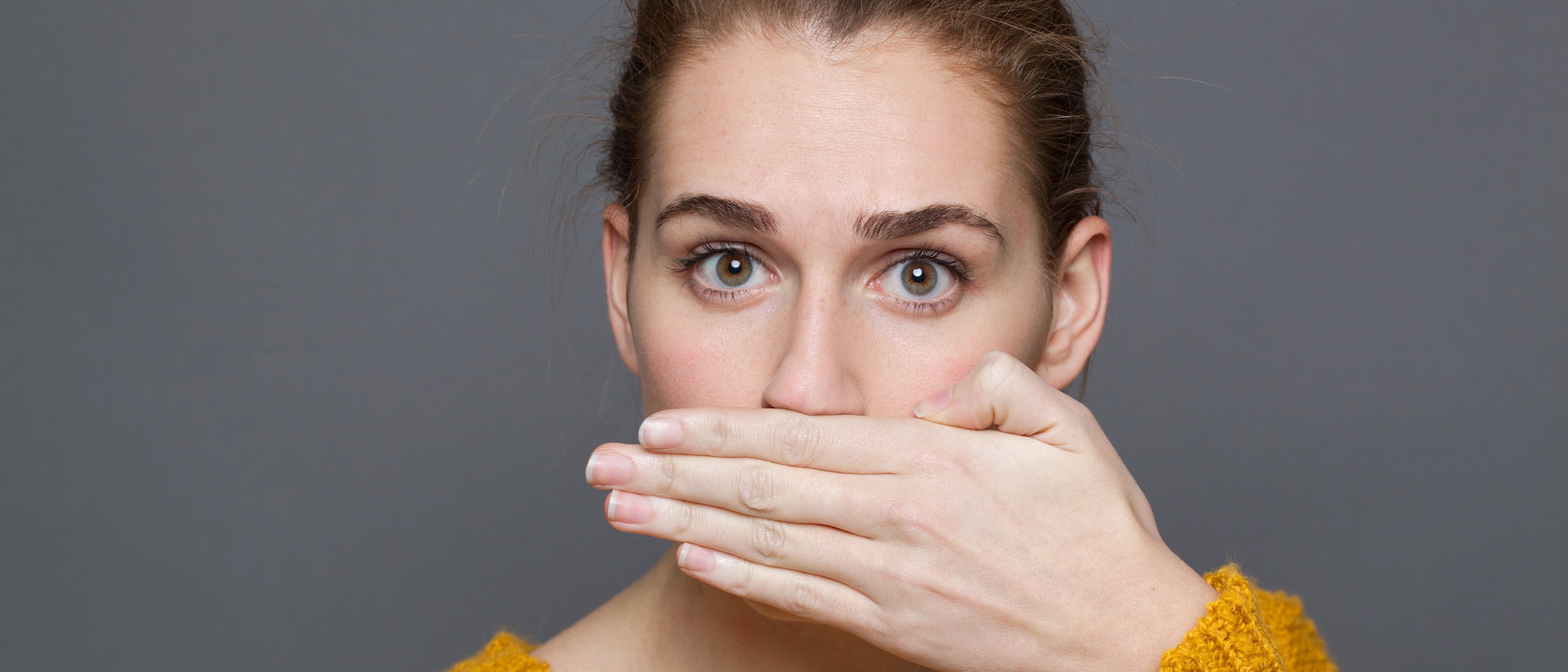 Young women covering her mouth with her hand indicating she has bad breath