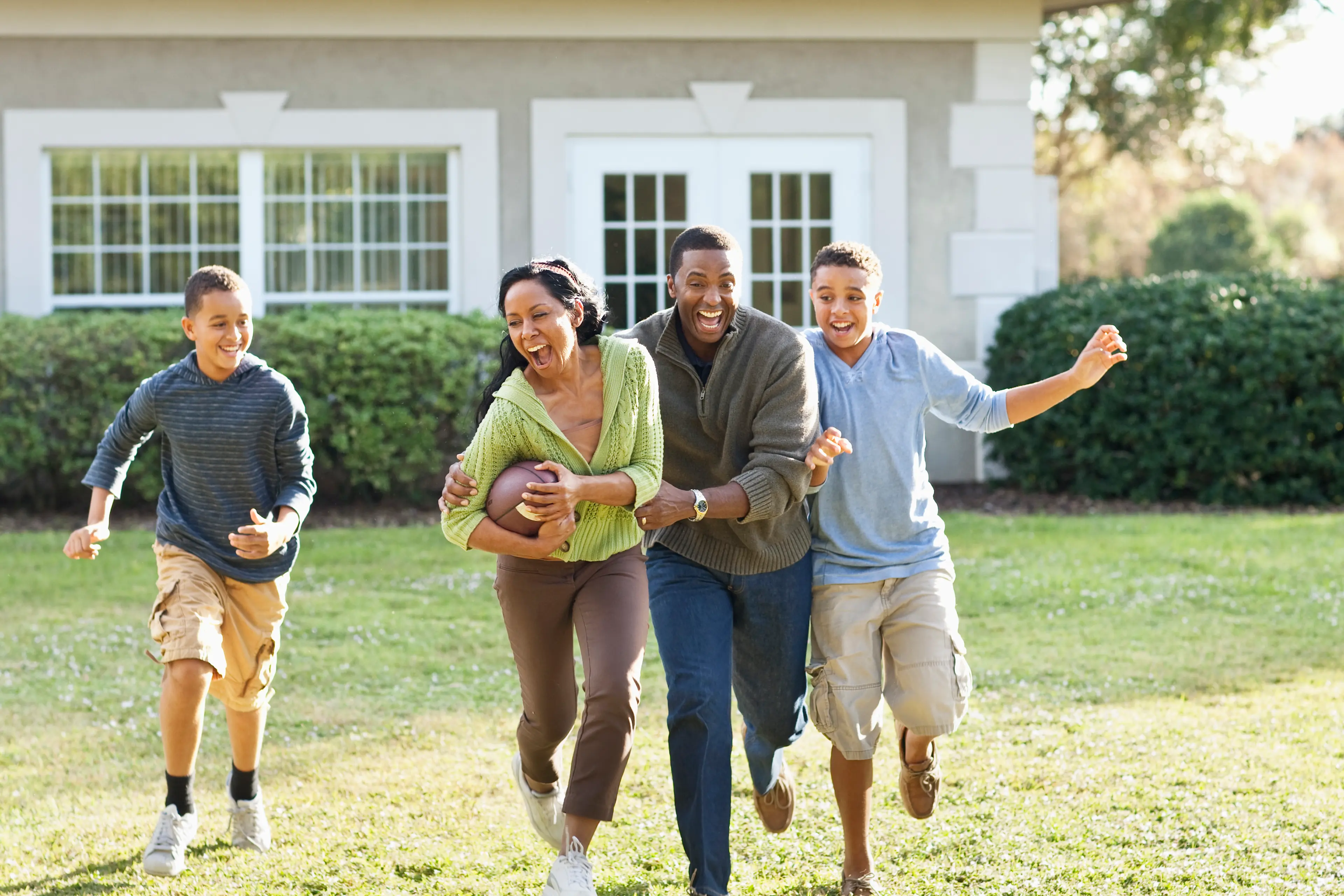Happy family playing football together in front of their home.