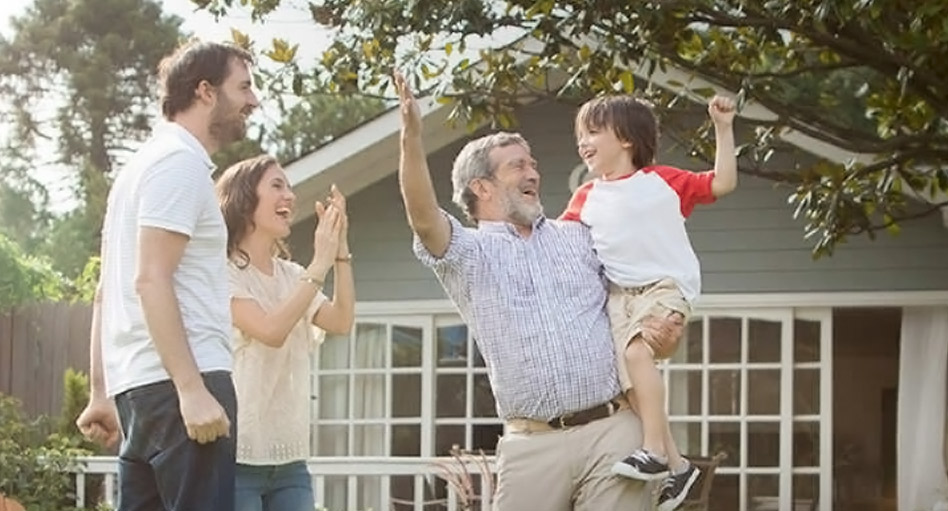 Grandfather playing with his grandson in the garden while the parents watch