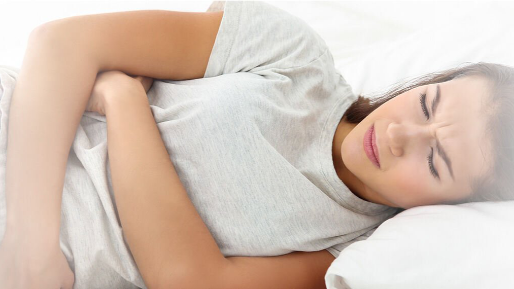 Woman lying on her side in bed with menstrual pain.