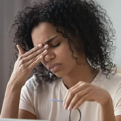 Femme assise, les yeux fermés, se tenant l'arête du nez de la main droite