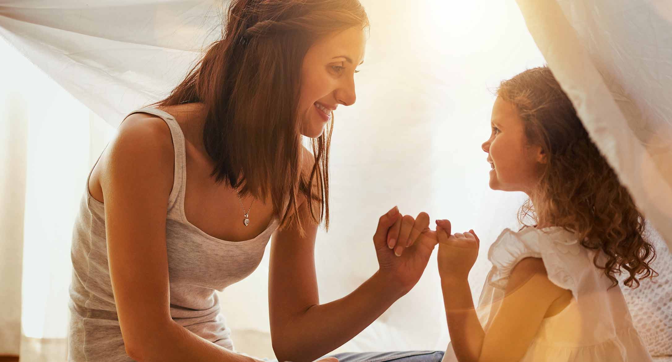 A mother and her daughter smiling at each other and holding pinkies