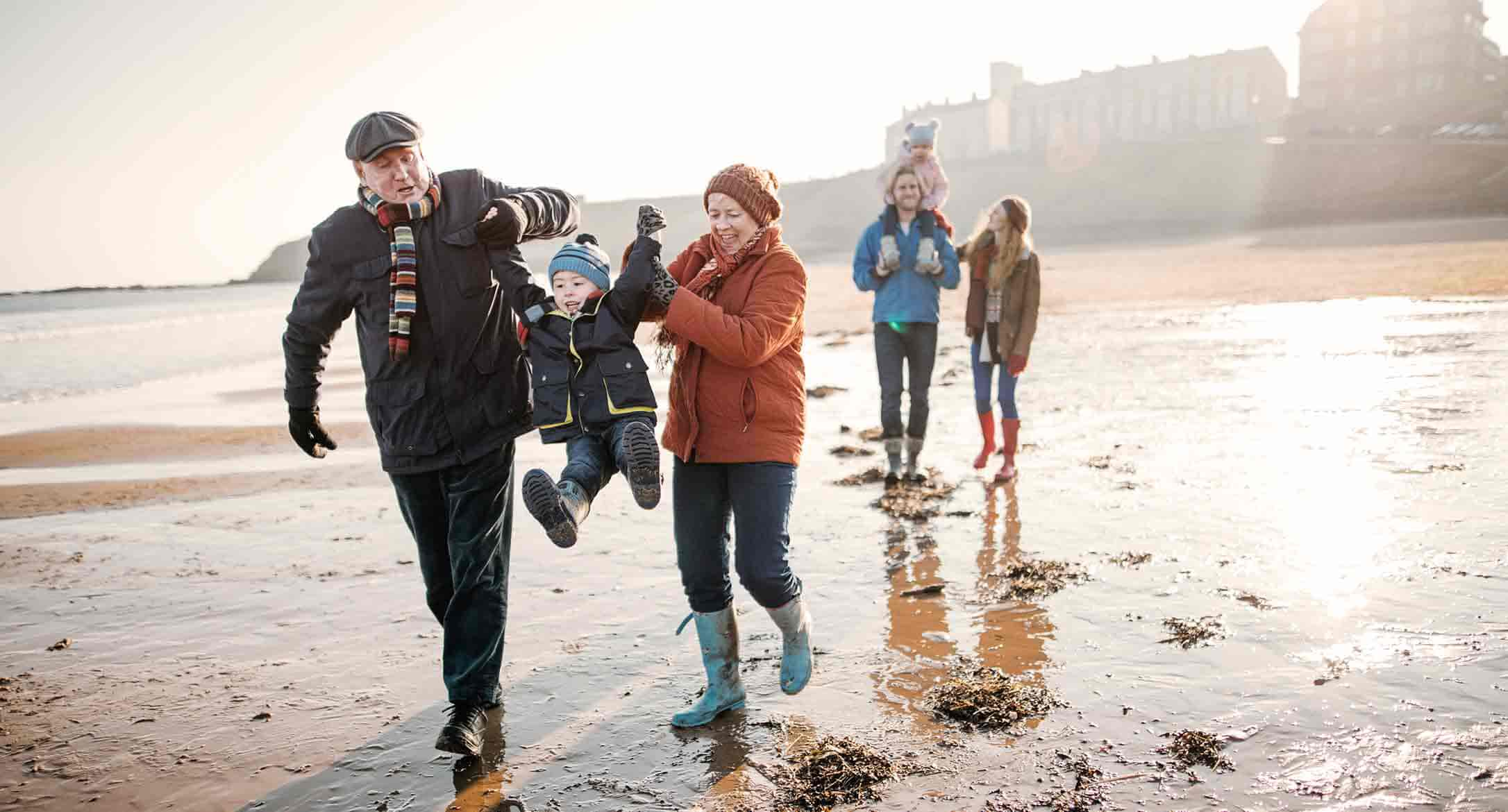 Multigeneration family with young kids walking along the beach