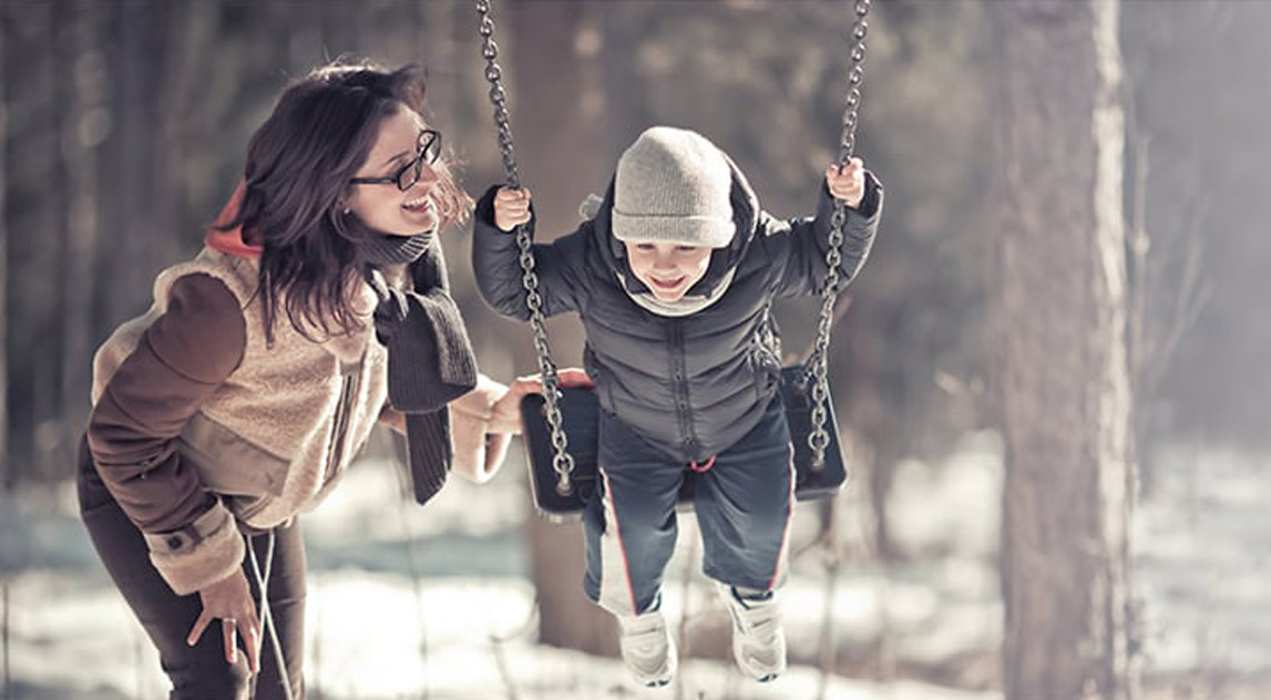 Mom pushing her son on a swing in the winter