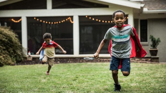 Two boys wearing capes and playing outside a house