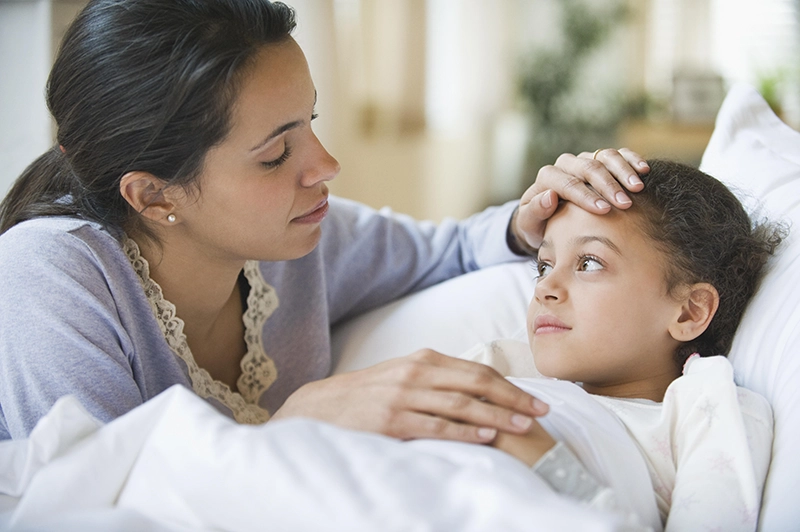 Mom checking her daughter's fever in bed