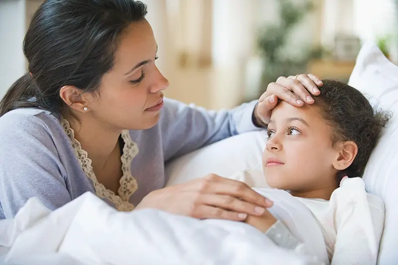 Mom checking her daughter's fever in bed