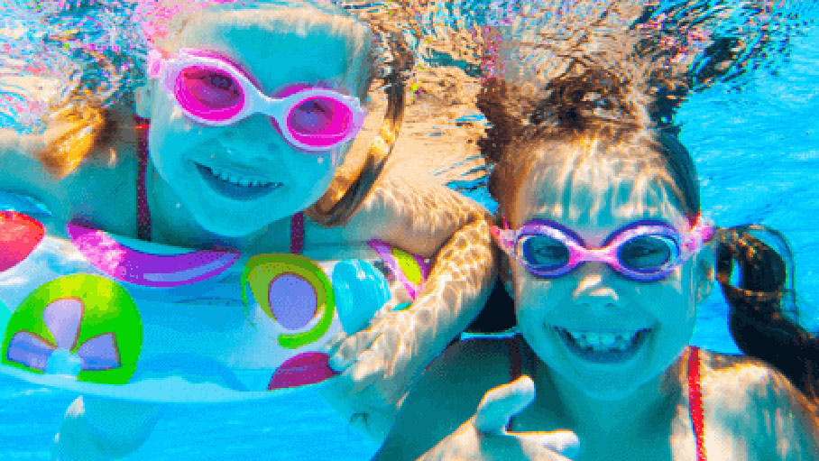 Two happy girls in goggles swimming under water.