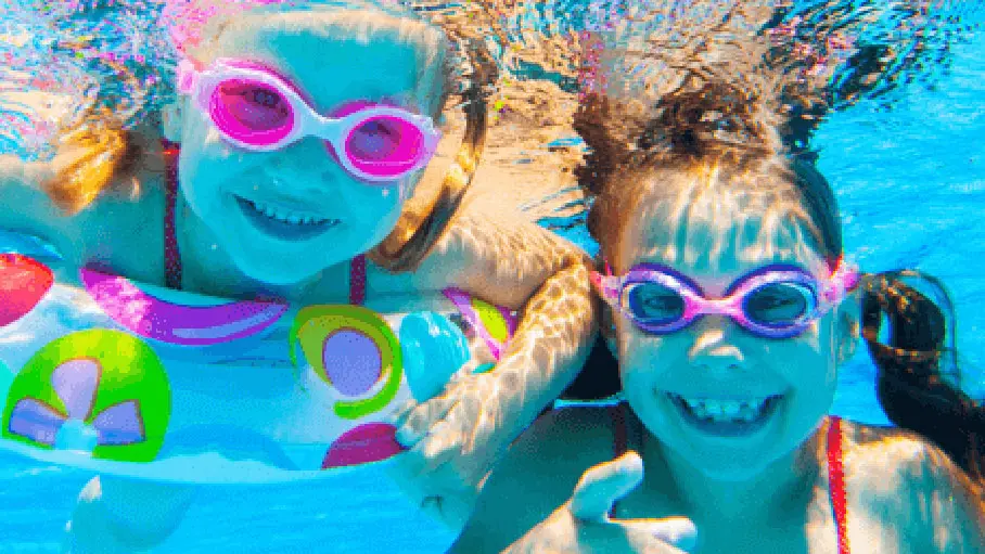 Two happy girls in goggles swimming under water.