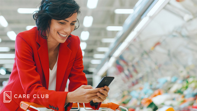 Happy woman holding her smart phone while leaning on a shopping card in a supermarket.