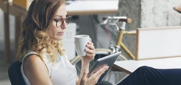 Femme qui lit sur une tablette, une tasse à la main