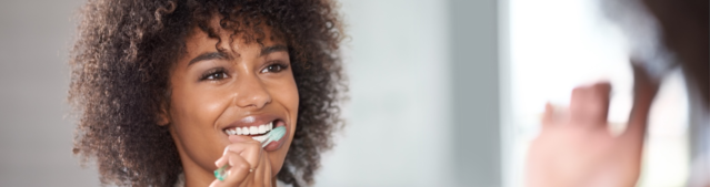 A young woman looking at the mirror and brushing her teeth.